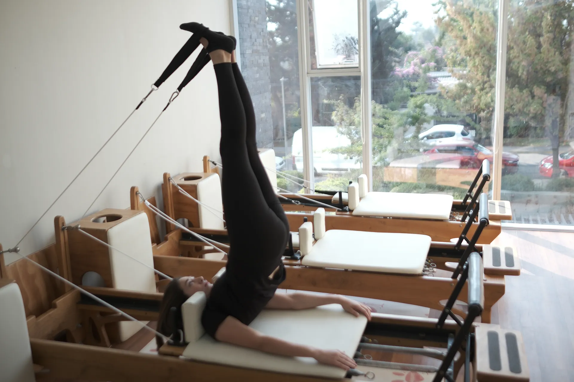 Alumna ejercitando en Reformer a contraluz frente a los árboles